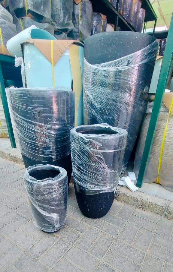 Tall and medium black plant pots wrapped in plastic, displayed outdoors on paving.