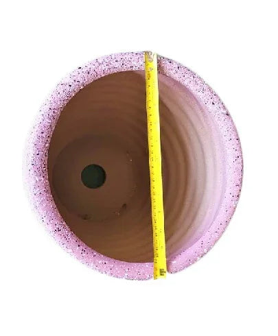 Top view of round pink plant pot with drainage hole and measuring tape across diameter