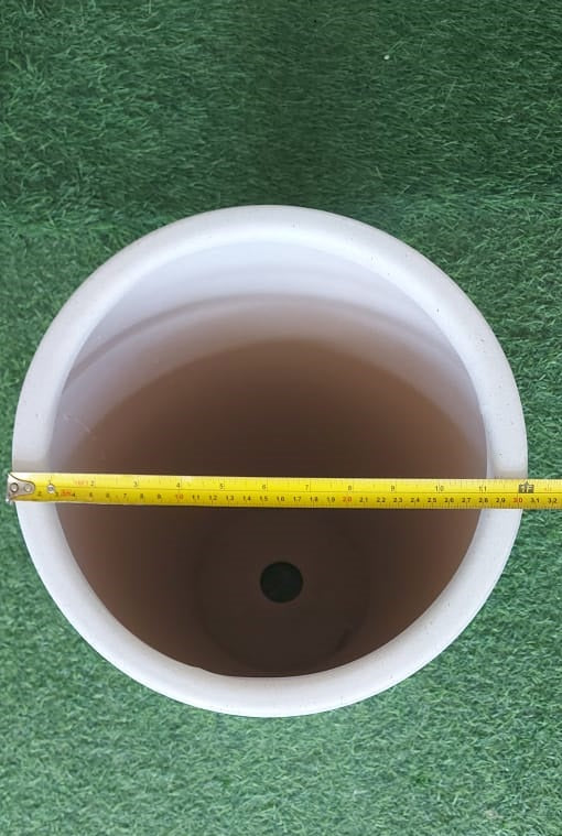 Top view of a round white plant pot with drainage hole and tape measure across the rim on grass