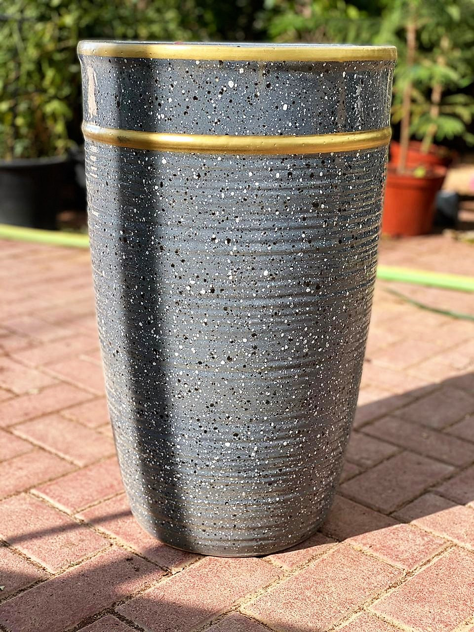 Large speckled ceramic planter pot with gold rim on outdoor brick patio