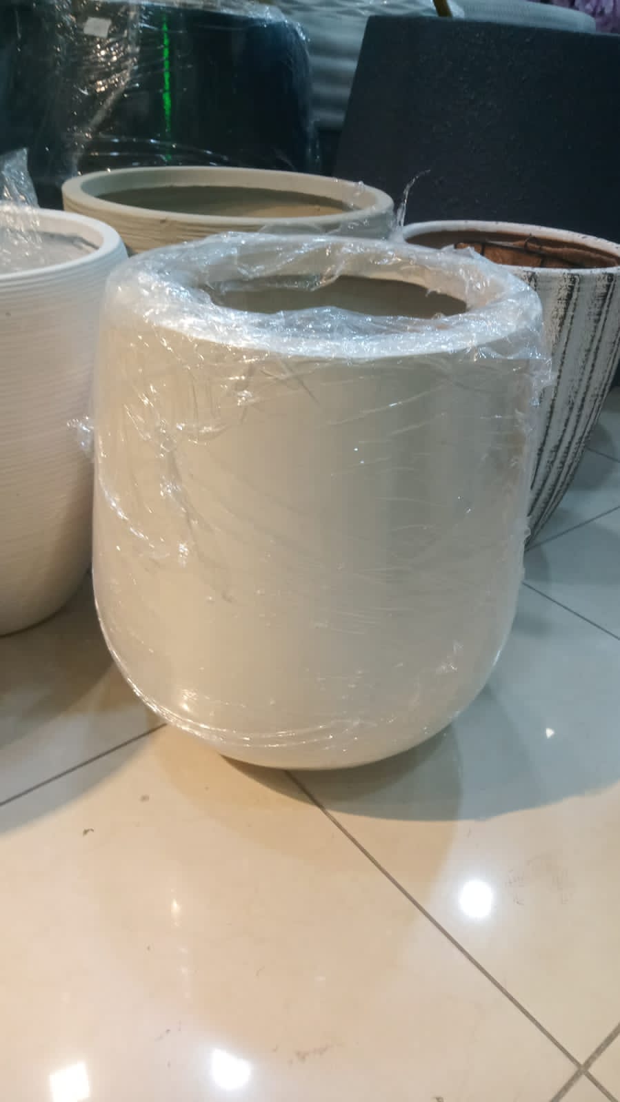 Large white round plant pot wrapped in plastic on tiled indoor floor