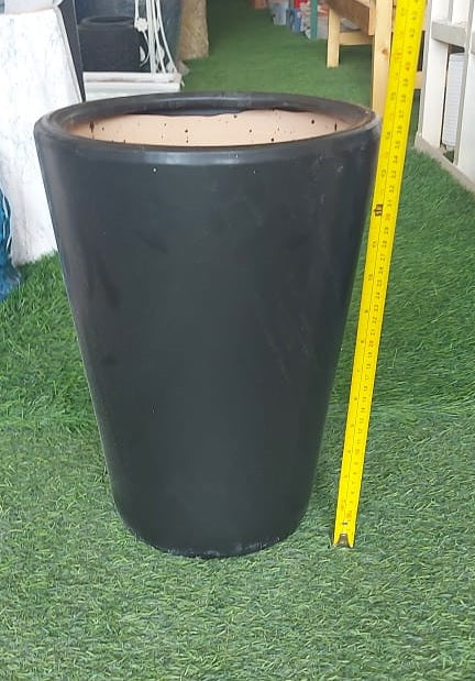 Tall black planter pot with measuring tape on artificial grass