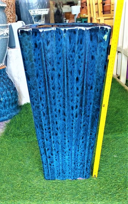 Tall blue ceramic planter vase with textured pattern on artificial grass, measuring tape beside