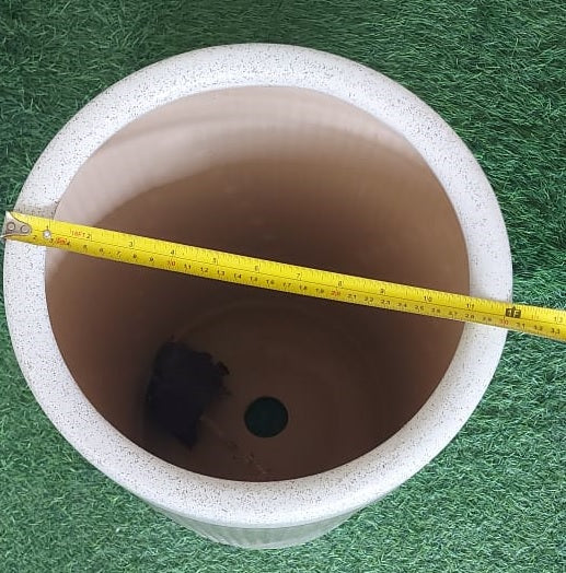 Top view of round plant pot with drainage hole, measuring tape across rim on green grass